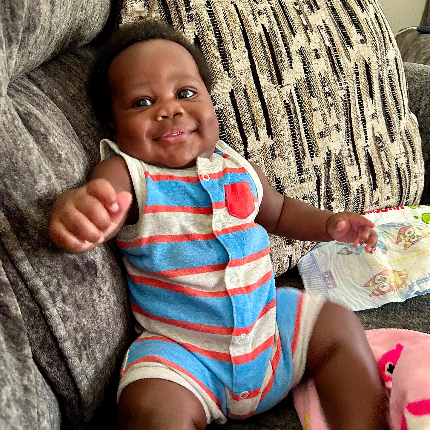 Jacari Flowers is registered to the contest to win money with this photo: baby, blanket, child, couch, cute, furniture, happy, home, indoor, infant, patterned, person, plush, portrait, reaching_out, romper, sitting, smiling, striped_clothing, young_child