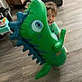 Ezra is registered to the contest to win money with this photo: blue, cabinet, casual_clothing, child, curly_hair, dinosaur, floor, fun, furniture, green, happy, indoor, inflatable, living_room, person, play, smile, toy, wood_floor, young