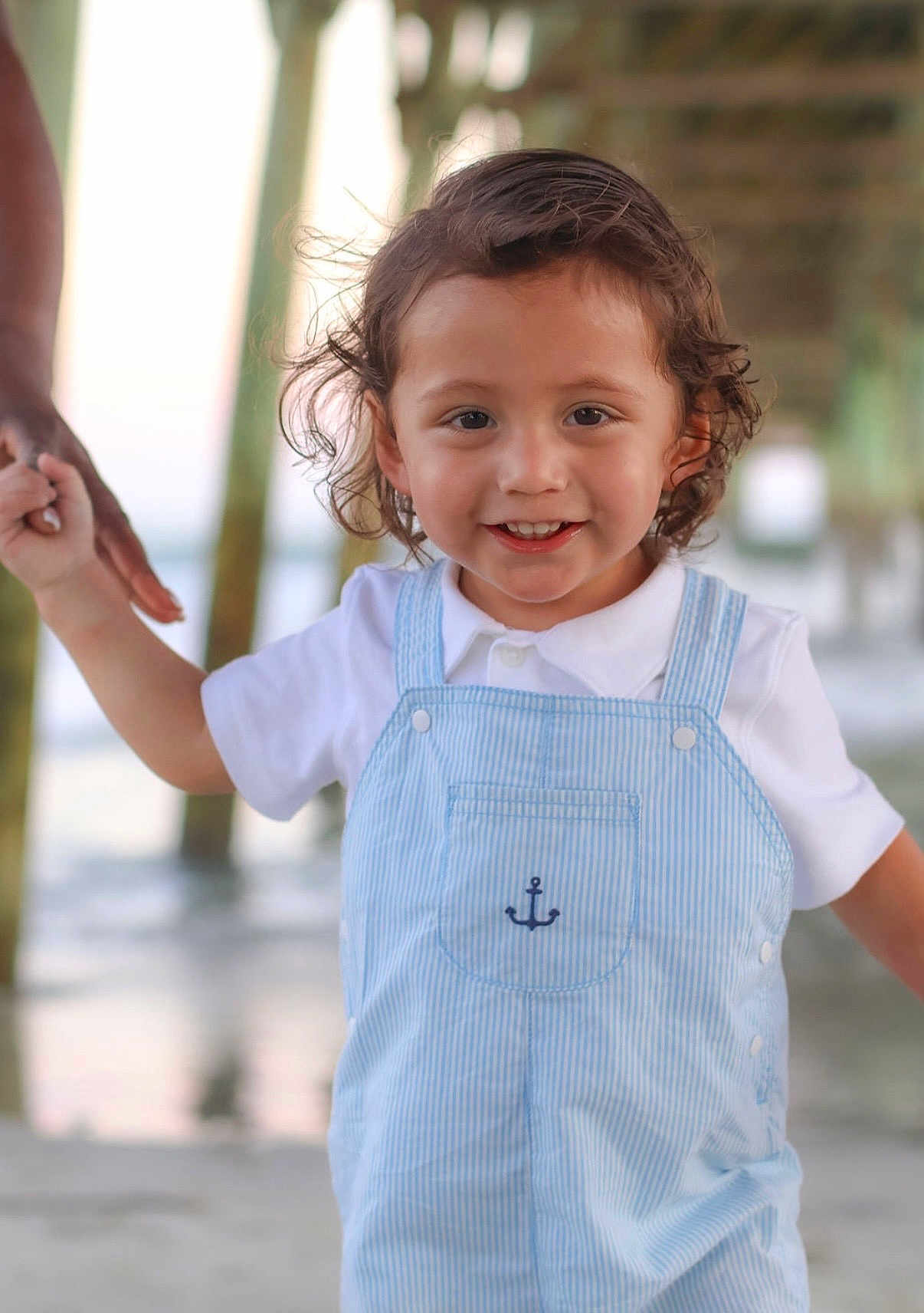 Ezra joined the competition — help win amazing prizes! toddler, child, smiling, curly_hair, holding_hand, overalls, white_shirt, outdoor, pier, water, beach, sunlight, happy, portrait, person, cute, young_child, summer, daylight, family