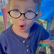 Michael joined the competition — help win amazing prizes! child, boy, glasses, blue_shirt, outdoor, expression, surprised, face, short_hair, standing, chair, table, grass, casual_clothing, daylight, person, young, curious, portrait, funny_face