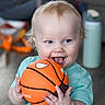 Wade is registered to the contest to win money with this photo: baby, basketball, blond_hair, blue_eyes, bokeh, child, couch, cute, expression, floor, hands, indoor, playful, portrait, smiling, teal_shirt, toddler, tongue_out, toy, water_bottle