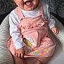 Alina is registered to the contest to win money with this photo: baby, smiling, pink_dress, sitting, baby_seat, cartoon_bear, flowers, tattoo, hand, nails, happy, infant, cute, clothing, face, child, indoors, couch, comfort, playful