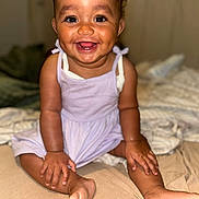 Lila a rejoint le concours — aidez-le/la à gagner de superbes lots ! baby, child, smiling, happy, dimple, dress, sitting, bed, indoors, skin, face, hands, feet, infant, person, cute, young, portrait, expression, cozy