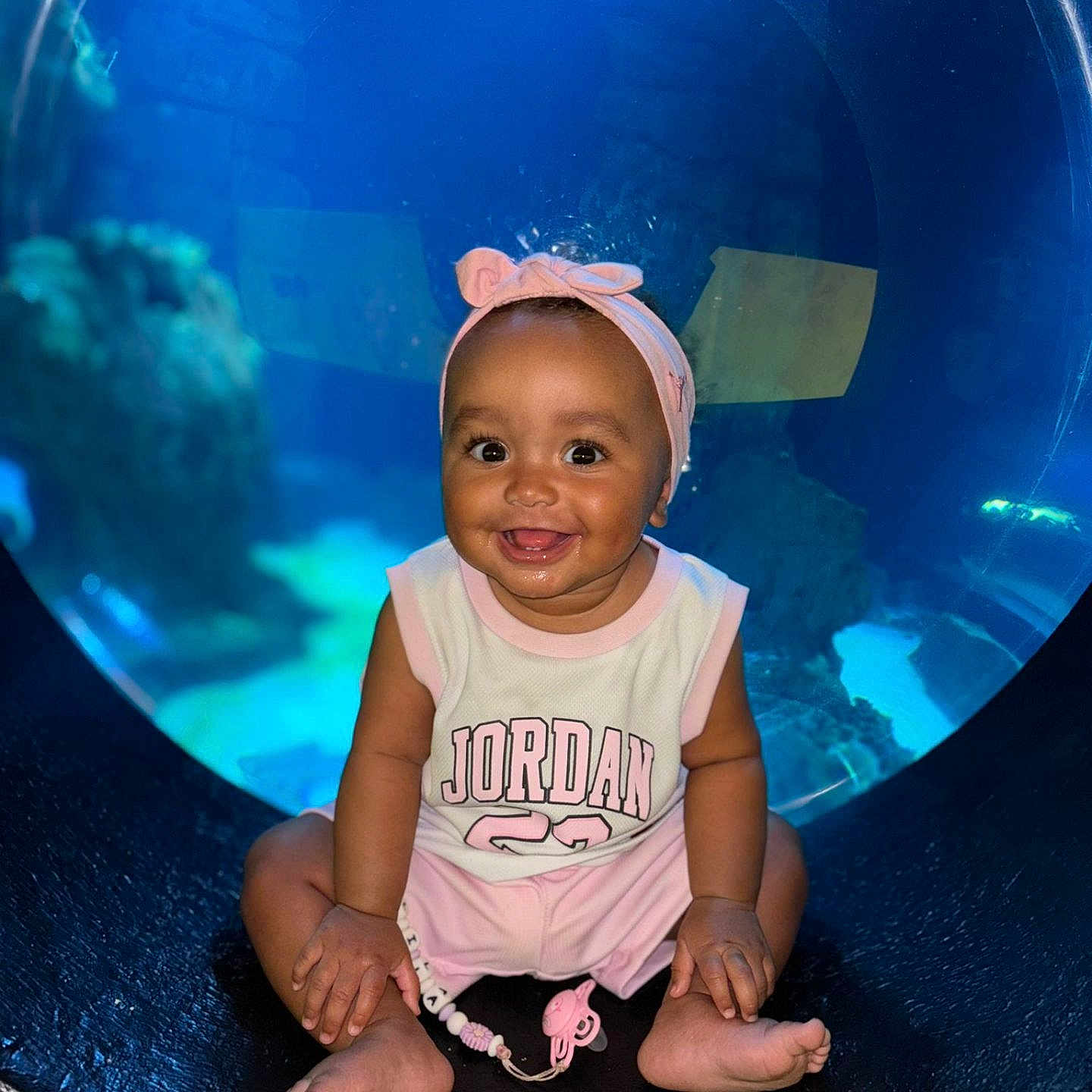 Lila participe au concours pour gagner de l'argent avec cette photo : aquarium, baby, bright, child, circular_window, cute, face, happy, headband, indoors, infant, pacifier, person, pink_clothing, playful, portrait, sitting, smiling, toy, underwater