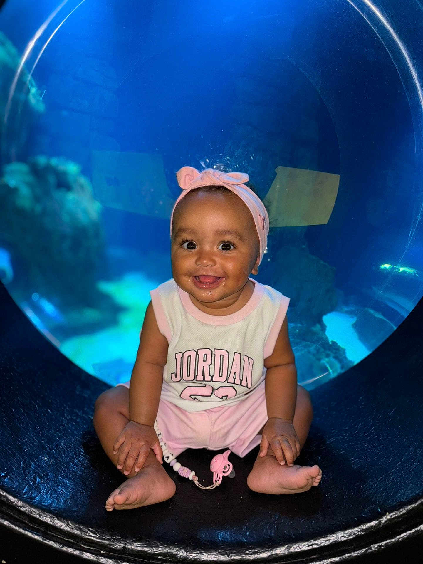 Lila participe au concours pour gagner de l'argent avec cette photo : baby, child, smiling, headband, pink_clothing, sitting, aquarium, underwater, circular_window, happy, cute, face, infant, indoors, playful, pacifier, toy, bright, portrait, person