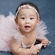 Madelyn joined the competition — help win amazing prizes! baby, child, portrait, smiling, happy, flower_headband, pink_dress, tulle, ruffles, toy, sitting, indoor, studio, blue_background, closeup, infant, fashion, cute, photography, soft_lighting
