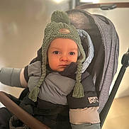 Noa a rejoint le concours — aidez-le/la à gagner de superbes lots ! baby, baby_transport, bundle_up, caucasian, child, cold_weather, headwear, indoors, jacket, knitted_hat, person, portrait, puffy_jacket, seated, serious_face, stroller, toddler, warm_clothing, winter_hat, young_child