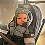 baby, baby_transport, bundle_up, caucasian, child, cold_weather, headwear, indoors, jacket, knitted_hat, person, portrait, puffy_jacket, seated, serious_face, stroller, toddler, warm_clothing, winter_hat, young_child