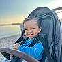 Noa a rejoint le concours — aidez-le/la à gagner de superbes lots ! baby, beach, blue_shirt, child, clothing, daylight, happy, nature, outdoor, person, portrait, relaxation, seat, seatbelt, smiling, stroller, sunset, toddler, vacation, young_child