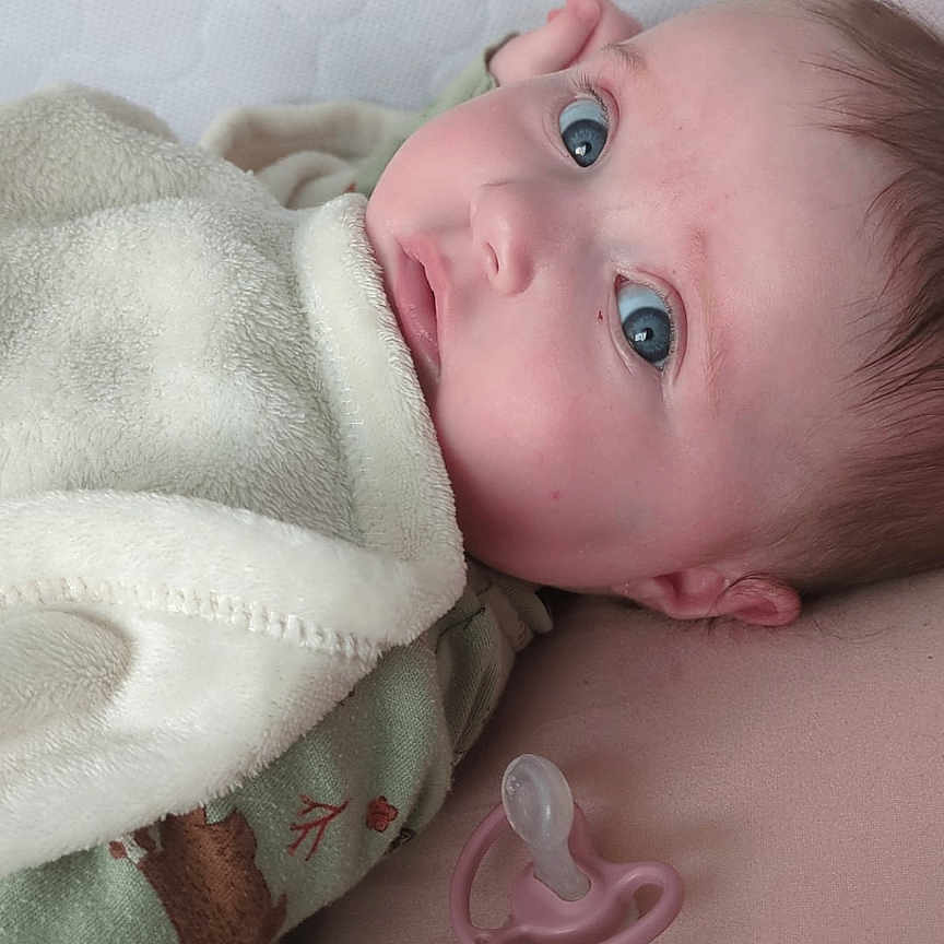 Justine a rejoint le concours — aidez-le/la à gagner de superbes lots ! baby, infant, blanket, pacifier, mattress, face, blue_eyes, lying_down, soft_texture, cozy, child, portrait, indoors, closeup, cute, sleepwear, expression, skin, head, newborn