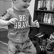 Raiden is registered to the contest to win money with this photo: child, toddler, boy, standing, walking, smiling, indoors, portrait, black_and_white, bookshelf, books, clothing, t_shirt, pants, wood_floor, shoes, home, playful, motion, face
