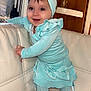 Summer a rejoint le concours — aidez-le/la à gagner de superbes lots ! baby, child, smile, headband, turquoise, dress, slippers, couch, indoor, window, wood_panel, happy, standing, person, furniture, cute, toddler, home, fabric, footwear