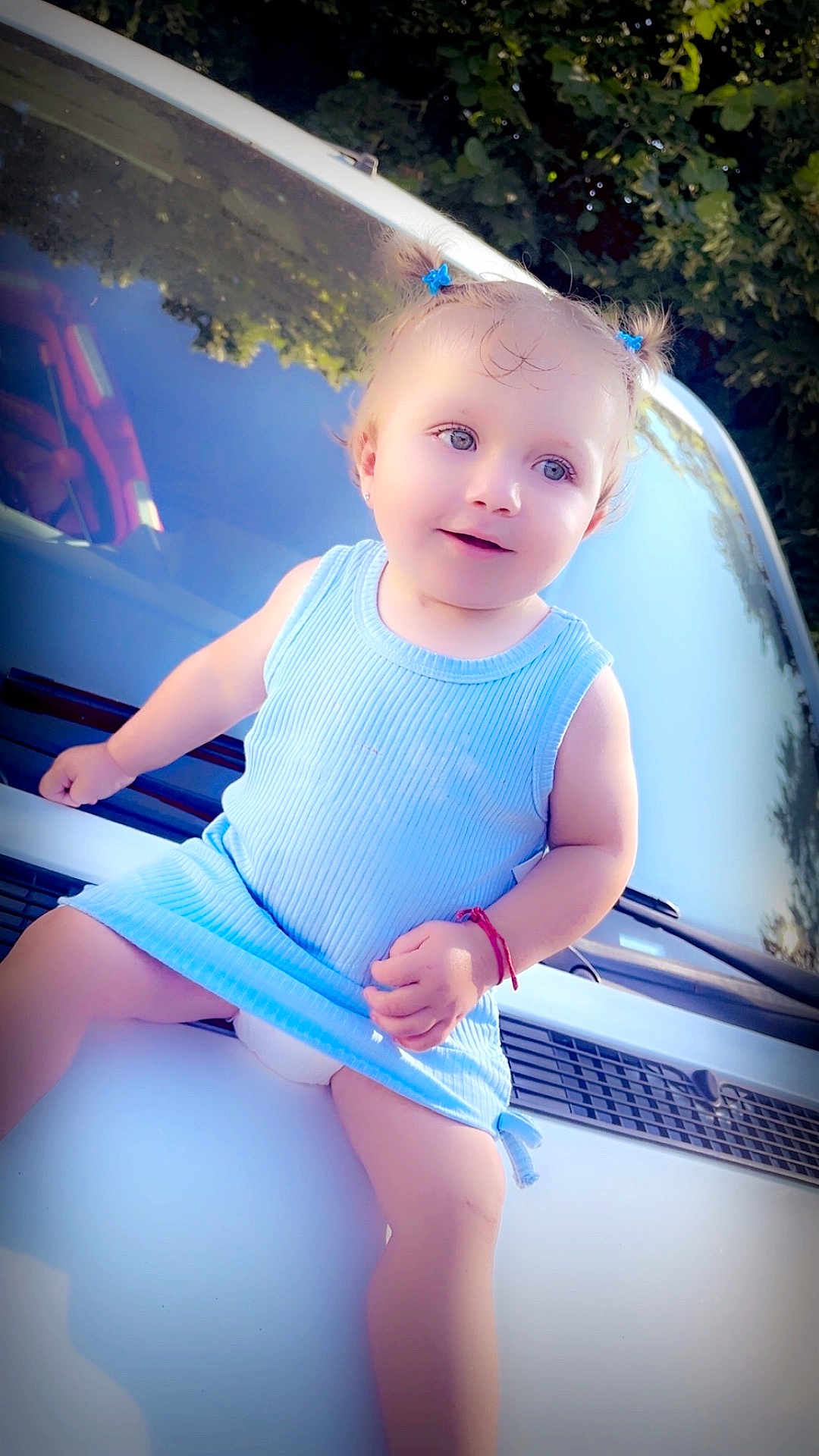 Summer a rejoint le concours — aidez-le/la à gagner de superbes lots ! toddler, child, blue_dress, car, car_hood, outdoor, smiling, hair_ties, baby, sunlight, reflection, trees, greenery, face, person, cute, happy, sitting, portrait, vehicle
