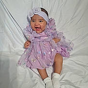 Kaylani Luna Lopez joined the competition — help win amazing prizes! baby, infant, smile, dress, headband, socks, sitting, happy, cute, portrait, child, fabric, white_background, clothing, toddler, young_child, indoors, person, sparkle, purple