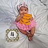 baby, infant, pink_tutu, headband, milestone_card, 4_months, white_sheet, cute, child, portrait, sitting, sign, orange_sign, adorable, clothing, smiling, hands, feet, young_child, indoor
