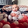 baby, ball_pit, balls, indoor, child, curious, seated, basket, blanket, soft_lighting, pink, white, red, playtime, cute, portrait, infant, toy, closeup, home