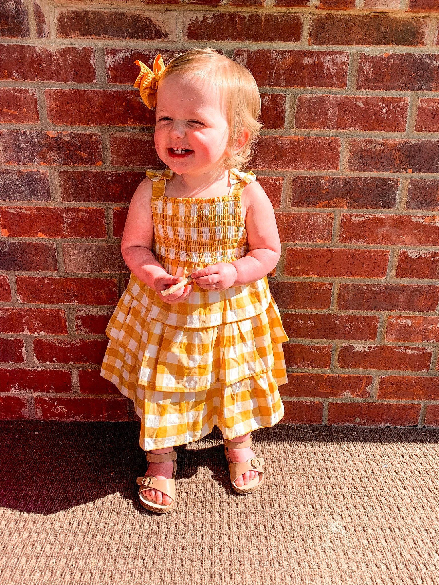 Roxanne is registered to the contest to win money with this photo: baby_toddler_clothing, brick, brickwork, child, day_dress, dress, hair, hand, happy, head, human_body, joy, one_piece_garment, orange, person, pink, plaid, sleeve, smile, standing