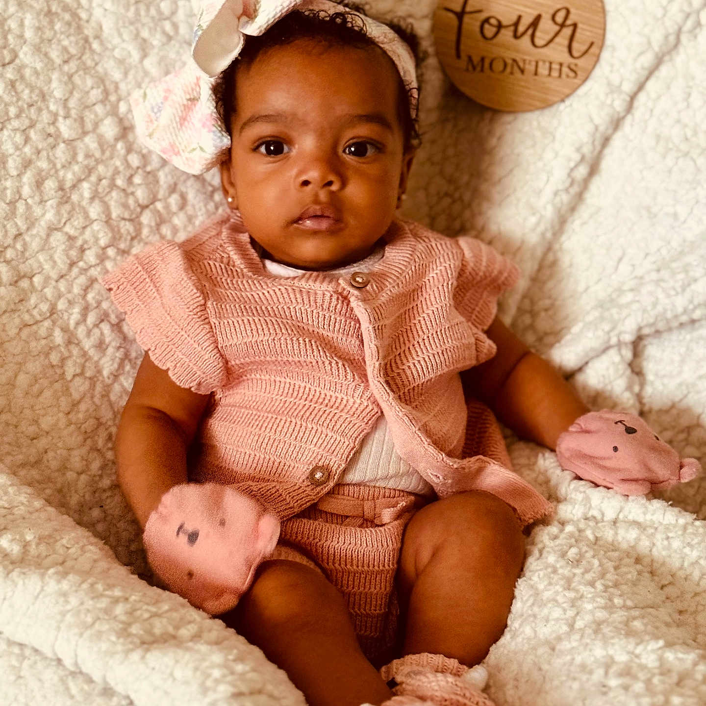 Iris is registered to the contest to win money with this photo: baby, blanket, bow, child, curly_hair, cute, four_months, headband, indoor, infant, knitted_outfit, mittens, pink_clothing, plush_texture, portrait, sitting, socks, soft_lighting, wooden_plaque, young_child