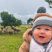 Maëlan participe au concours pour gagner de l'argent avec cette photo : baby, child, smiling, hat, winter_clothing, jacket, bib, outdoor, field, grass, sheep, trees, nature, cloudy_sky, portrait, happy, closeup, person, infant, seasonal