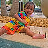 toddler, child, poolside, water, wet, smiling, colorful_clothing, umbrella, palm_trees, outdoor, summer, happy, sitting, playful, vacation, sunny, nature, fun, portrait, daytime