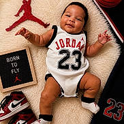 Dylan joined the competition — help win amazing prizes! baby, infant, basketball, jordan, sneakers, sportswear, sign, text, smiling, black_hair, white_outfit, red, black, white, sock, rug, toy, child, portrait, indoor