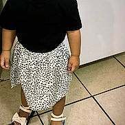 Emma is registered to the contest to win money with this photo: child, toddler, portrait, standing, pacifier, smiling, black_shirt, polka_dot_skirt, sandals, bows, fashion, indoors, tiled_floor, home, wall, full_body, young_child, dark_hair, hair_bows, casual_clothing