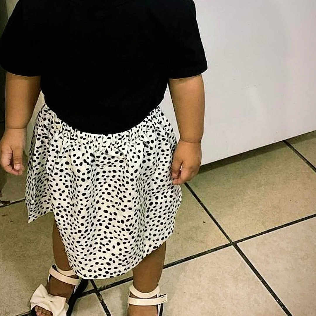 Emma is registered to the contest to win money with this photo: child, toddler, portrait, standing, pacifier, smiling, black_shirt, polka_dot_skirt, sandals, bows, fashion, indoors, tiled_floor, home, wall, full_body, young_child, dark_hair, hair_bows, casual_clothing