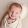 baby, newborn, swaddled, blanket, sleeping, smile, infant, portrait, closeup, hand, face, head, pillow, soft_texture, cozy, peaceful, nursery, skin, cute, warm_lighting