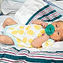 newborn, baby, pacifier, hospital_bassinet, onesie, lemon_pattern, socks, blanket, striped_blanket, infant, lying_down, baby_clothing, hospital, sleepy, cute, small_arms, small_legs, skin, face, resting