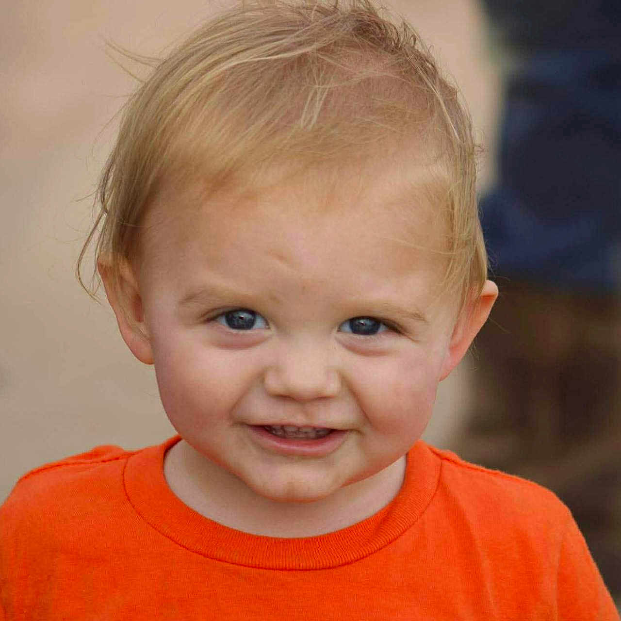 Asher is registered to the contest to win money with this photo: child, toddler, smile, orange_shirt, blonde_hair, blue_eyes, face, portrait, outdoor, happy, person, casual_clothing, cute, young_child, head_and_shoulders, expression, skin, baby, background_blur, standing