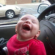 Jordyn joined the competition — help win amazing prizes! baby, laughing, car_interior, red_clothing, child, happy, person, seat, steering_wheel, window, vehicle, parking_lot, car, joy, smile, head, face, infant, clothing, transport
