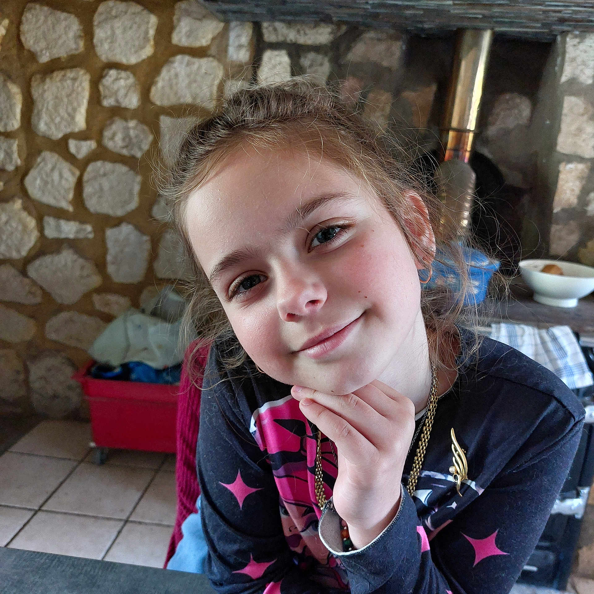 Anais participe au concours pour gagner de l'argent avec cette photo : child, girl, smile, face, hand, indoor, stone_wall, necklace, long_hair, earrings, casual_clothing, portrait, young, cute, person, fashion, jewelry, expression, seated, tile_floor