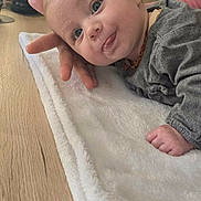 Ambre participe au concours pour gagner de l'argent avec cette photo : baby, infant, child, hand, blanket, wooden_table, plant, beverage_container, indoor, curious_expression, tongue_out, soft_texture, casual_clothing, face, portrait, person, home_interior, natural_light, supporting_hand, close_up