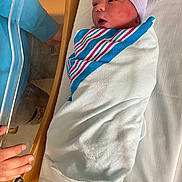 Charles is registered to the contest to win money with this photo: newborn, baby, hospital, blanket, bassinet, infant, swaddled, bed, person, hat, hand, medical, healthcare, cute, sleeping, newborn_care, striped_hat, soft, tender, resting