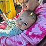 baby, woman, child, car, seat, pink_hoodie, tie_dye, holding, affection, love, portrait, casual_clothing, indoor, seatbelt, glasses, sunlight, face, head, earrings, candid