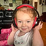 toddler, child, headphones, smile, indoor, living_room, furniture, couch, pink_chair, wall_art, tiger_drawing, person, cute, happy, casual_clothing, table, head, face, playful, cozy