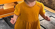 Ellie is registered to the contest to win money with this photo: carpet, casual, child, coffee_table, couch, curious, expression, floor, furniture, home, indoor, living_room, person, portrait, socks, standing, toddler, toy, yellow_dress, young_child