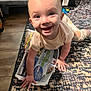 baby, carpet, child, clothing, crawling, eyes, floor, furniture, hand, happy, head, indoor, mouth, newspaper, pattern, person, play, smiling, toy, wood_floor