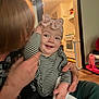 Ellie is registered to the contest to win money with this photo: baby, child, person, headband, striped_clothing, smile, indoor, adult, hand, kitchen, light_fixture, floor, toy, blanket, holding, happy, face, home, warm_lighting, cozy