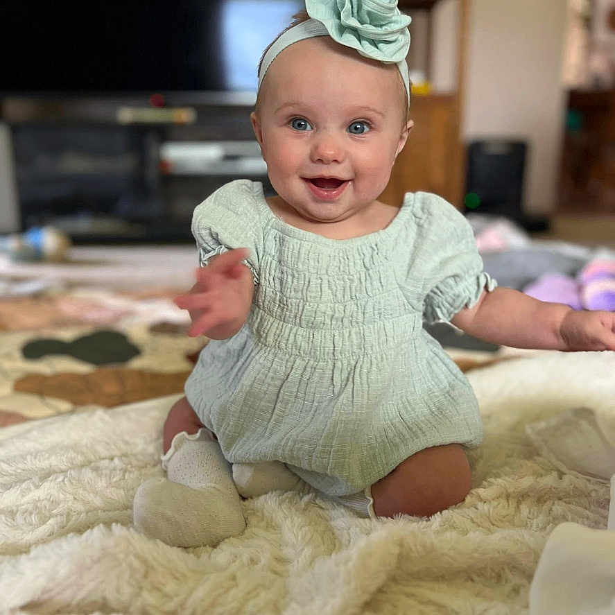 Amelia joined the competition — help win amazing prizes! baby, blanket, child, cozy, cute, dress, flower, happy, headband, home, indoors, infant, living_room, person, portrait, sitting, smiling, sock, soft_texture, young_child