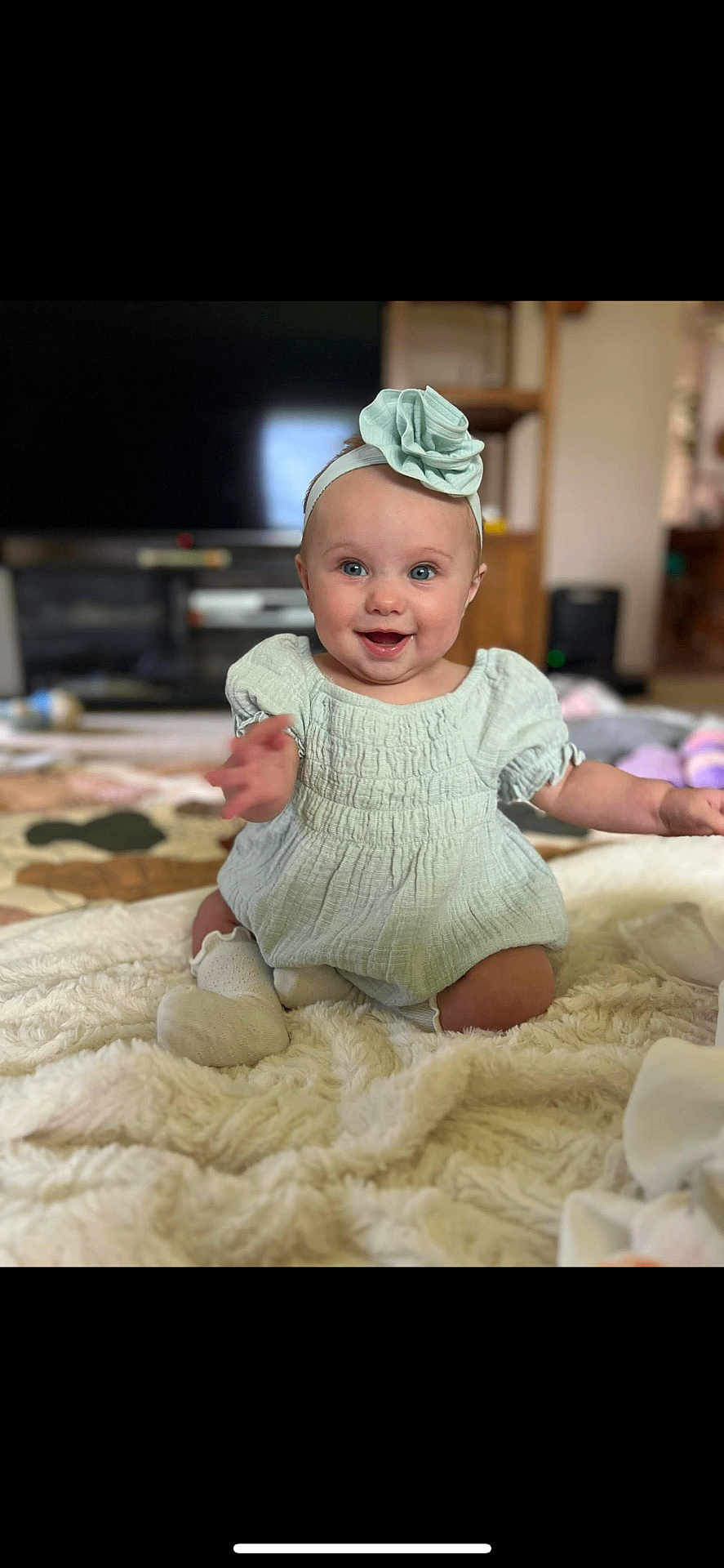 Amelia joined the competition — help win amazing prizes! baby, child, smiling, headband, flower, dress, sitting, blanket, indoors, living_room, cute, happy, person, infant, soft_texture, sock, young_child, portrait, home, cozy