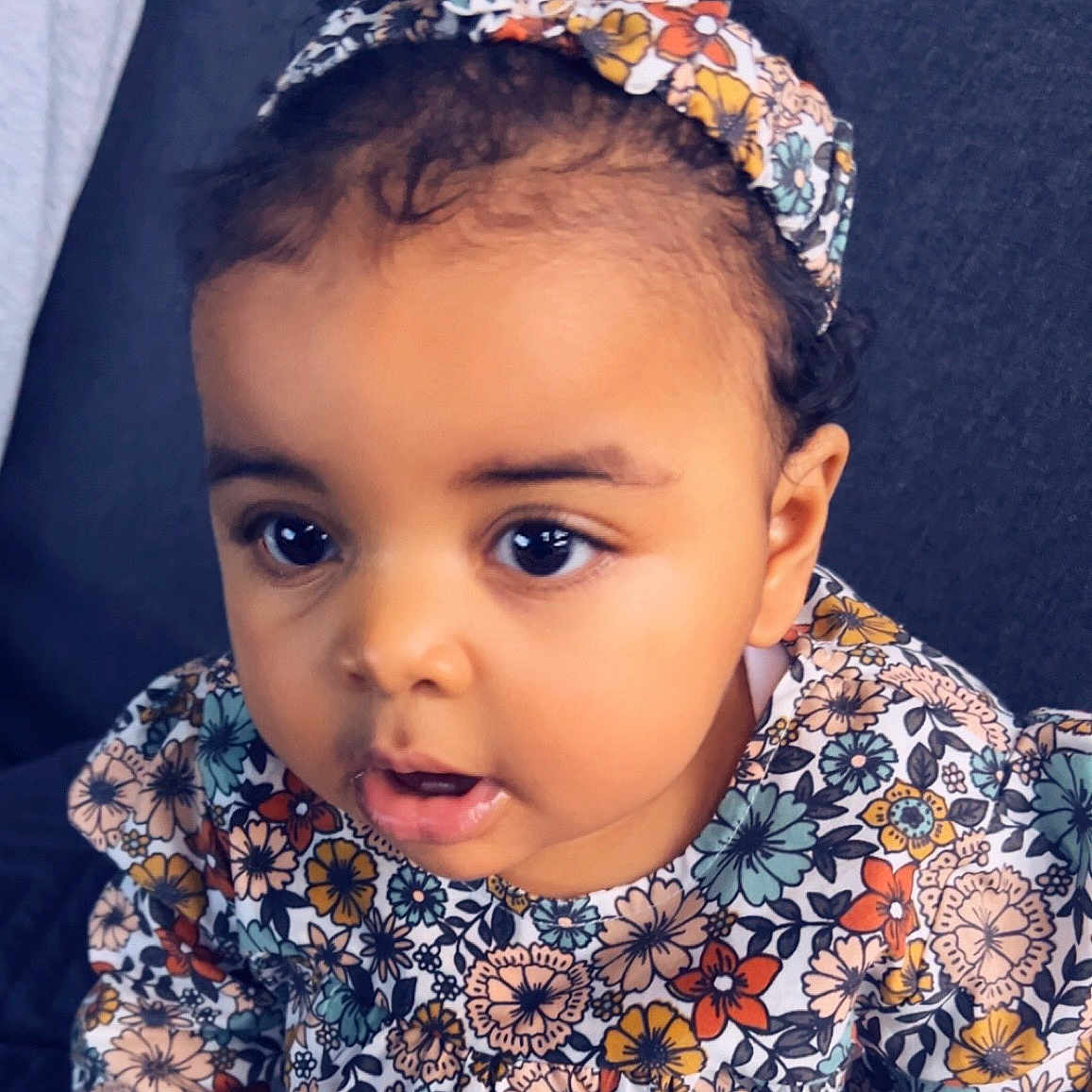 Amy-Laïyla a rejoint le concours — aidez-le/la à gagner de superbes lots ! baby, child, colorful, couch, curly_hair, cute, expression, eyes, fabric, face, floral, girl, headband, indoor, mouth, patterned_clothing, person, portrait, sitting, young_child