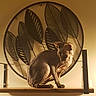 Uby a rejoint le concours — aidez-le/la à gagner de superbes lots ! sphynx_cat, cat, hairless_cat, pet, animal, indoor, decor, metal_art, leaf_pattern, wooden_shelf, warm_lighting, wall, feline, sitting, shadow, home, cozy, quiet, portrait, artistic