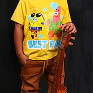 Jesús David joined the competition — help win amazing prizes! child, boy, yellow_tshirt, spongebob, patrick_star, guitar, musical_instrument, brown_pants, sneakers, standing, smiling, portrait, studio, black_background, casual_clothing, happy, cute, young, indoors, fashion