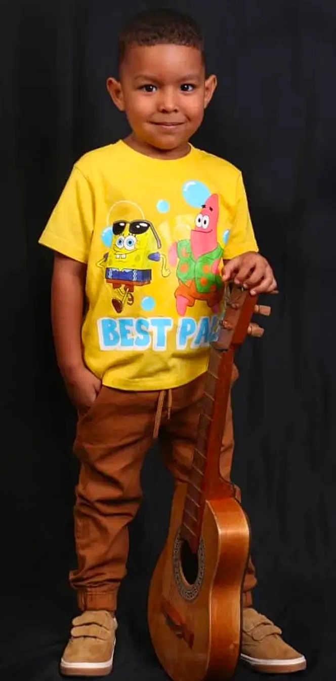 Jesús David joined the competition — help win amazing prizes! child, boy, yellow_tshirt, spongebob, patrick_star, guitar, musical_instrument, brown_pants, sneakers, standing, smiling, portrait, studio, black_background, casual_clothing, happy, cute, young, indoors, fashion