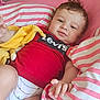 Reda participe au concours pour gagner de l'argent avec cette photo : baby, child, infant, red_shirt, levi's, yellow_toy, striped_bedding, pink_bedding, white_bedding, bed, relaxed, smiling, indoors, cute, person, portrait, hand, face, lying_down, soft_toy