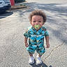 Alexander is registered to the contest to win money with this photo: toddler, child, pacifier, curly_hair, tropical_outfit, shorts, shirt, sneakers, outdoor, parking_lot, sunny, shadow, asphalt, smiling, person, standing, daylight, casual_clothing, happy, urban