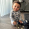 toddler, child, dinosaur_pajamas, sitting, wooden_floor, crumbs, food, indoors, natural_light, curly_hair, cozy, cute, expression, face, socks, carpet, home, window_blinds, flooring, person