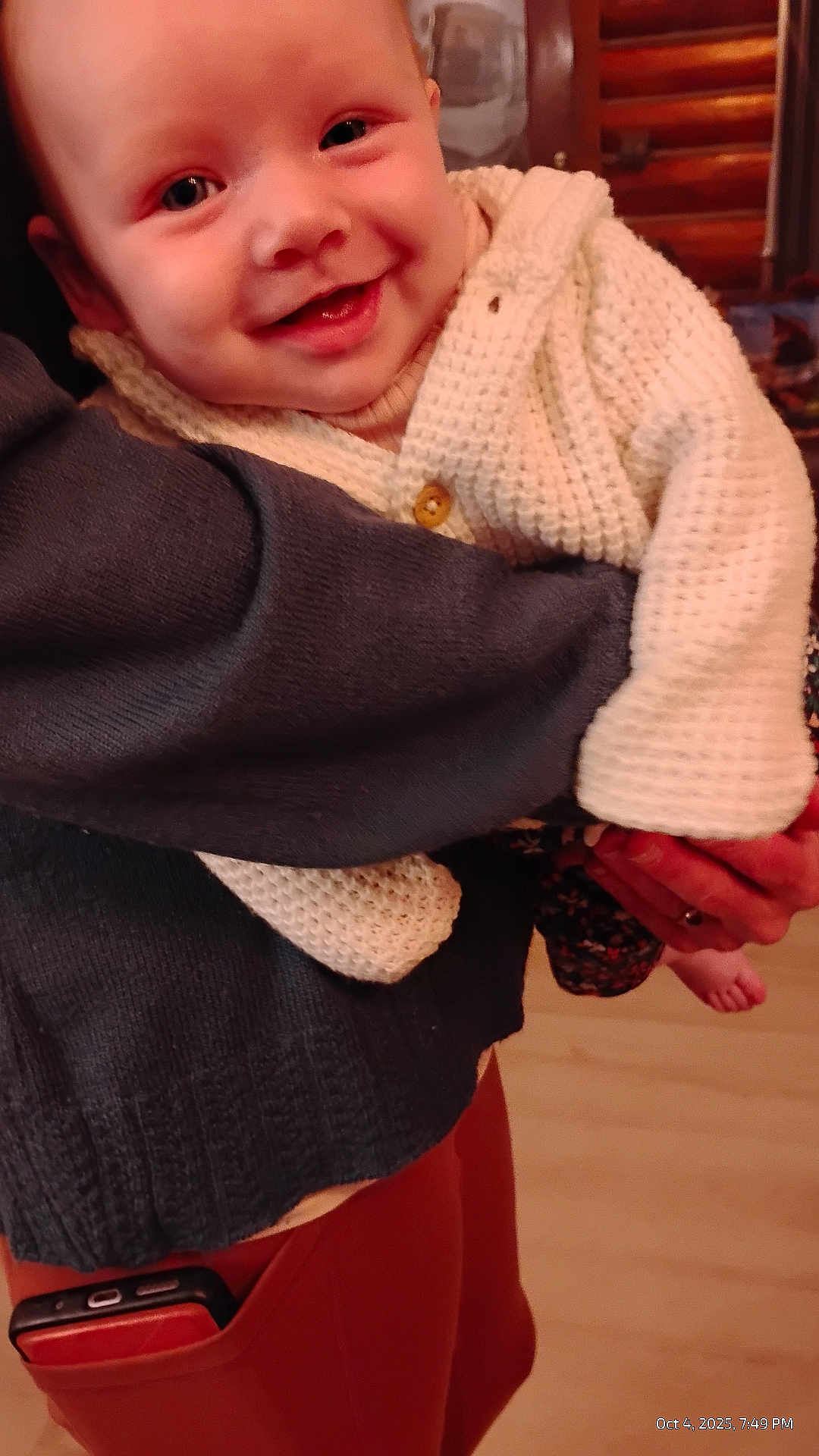 Ruby-Rose joined the competition — help win amazing prizes! baby, smile, sweater, knitwear, holding, adult, hand, indoor, person, face, happy, clothing, phone, pocket, pants, warm_lighting, closeup, child, infant, cozy