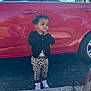 toddler, child, car, red_car, pavement, sidewalk, reflection, black_cardigan, leopard_print_pants, white_shoes, outdoor, playful_expression, curly_hair, earrings, person, photography, daylight, parking_lot, keys, handbag